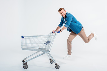 Happy young man running with shopping trolley and smiling at camera © LIGHTFIELD STUDIOS
