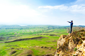 Young man on top of rock cliff pointing away by hand