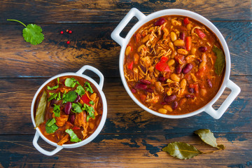 Turkey chili, ,stewed with beans, tomatoes, bell pepper, onion, garlic, thyme, cinnamon, chocolate and fresh cilantro, in white bowl and casserole on wooden table. - 137762820