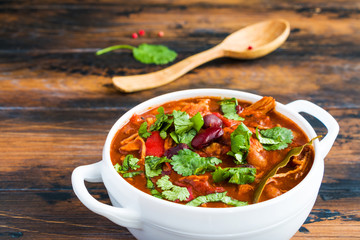 Turkey Chili. Stewed with black and white beans, tomatoes, bell pepper, onion, garlic, thyme, cinnamon, chocolate and fresh cilantro. Soup bowl on wooden table.