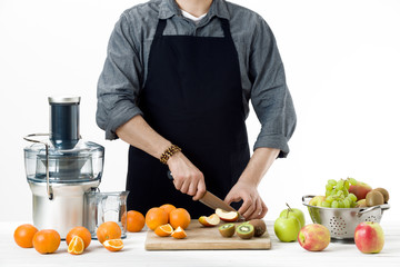 Anonymous man wearing an apron, preparing healthy freshly made fruit juice, using modern electric juicer, healthy lifestyle concept on white background - obrazy, fototapety, plakaty