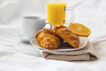 Bed breakfast with coffee cup, croissants and orange juice on white sheets