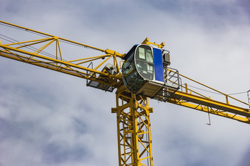 Construction tower crane, cabin, closeup, on blue sky with clouds.