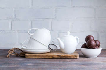 Fototapeta na wymiar White porcelain tea cup and saucer, teapot and strainer, chocolates on wooden desk against white background. Copy space.