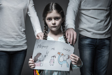 Little sad girl standing between her parents