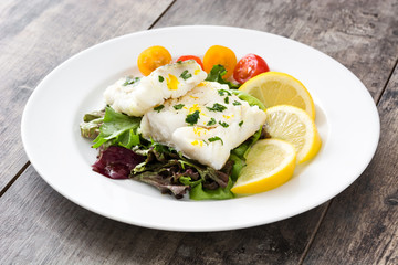 Fried cod fillet and salad in plate on wooden background
