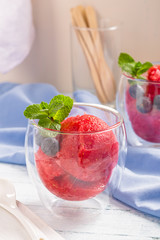 Fruit strawberry sorbet with blueberry and mint in glass on table. 