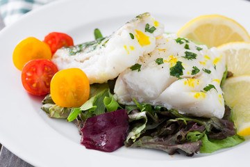Fried cod fillet and salad in plate on wooden background
