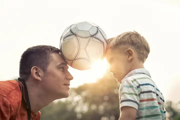Poster Im Rahmen Father and son playing football in park at sunny day © Andrii IURLOV