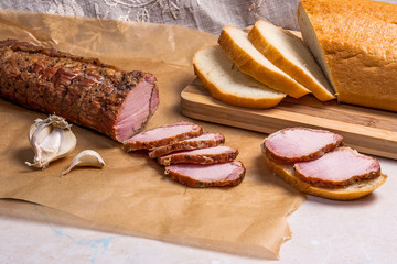 Slice smoked meat or ham, garlic and white wheat bread on brown packing paper.