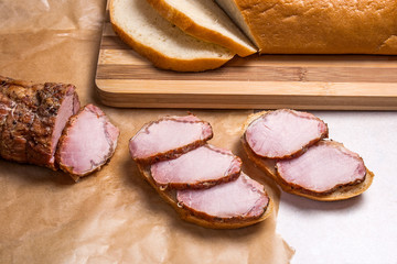 Slices smoked meat or ham on brown packing paper. Slices white wheat bread on wooden cutting board.