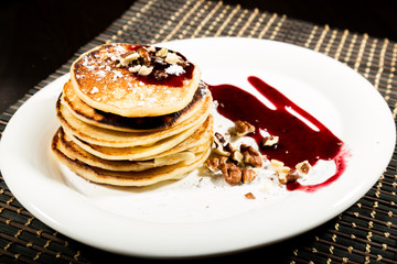 Homemade sweet pancakes with fruit jam on a white plate. Breakfast with stack topped blueberry jam and walnuts.