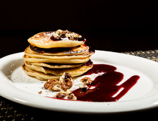 Homemade sweet pancakes with fruit jam on a white plate. Breakfast with stack topped blueberry jam and walnuts.