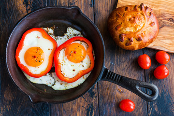 Fried eggs and bell pepper in black iron-cast skillet, fresh tomatoes and bread. Top view.