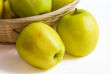 Pommes Golden devant une corbeille sur fond blanc