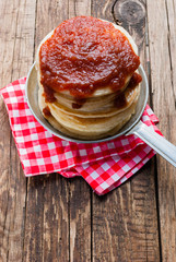 Stack of pancakes with apple jam on wooden background. Red napkin and cutlery.