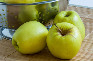 Pommes Golden devant une écumoire sur fond de bambou