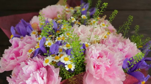 Rotating bouquet of flowers. Peonies, irises, chamomiles on wooden background (close-up)