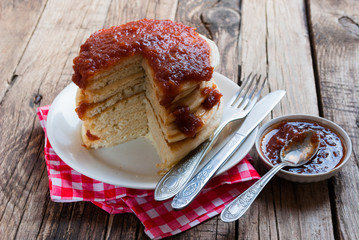 Stack of pancakes with apple jam on wooden background. Red napkin and cutlery.