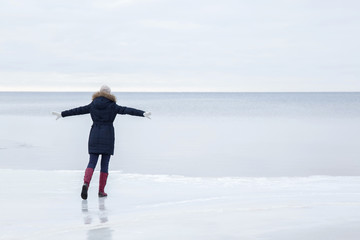 Young woman on the ice at the seashore feels the freedom in winter afternoon.