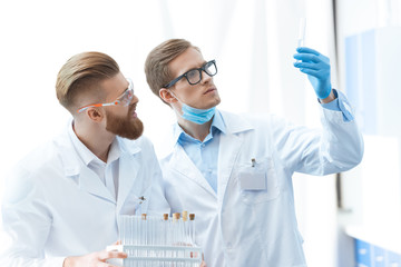Young men chemists in glasses looking at test tube in laboratory