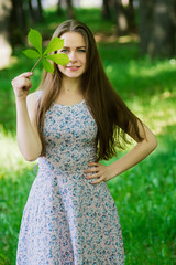 Smiling brunette girl hiding face by leaf.