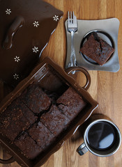 Chocolate brownies in a ceramic form. Piece of cake and coffee in a metal cup and saucer
