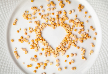 Yellow dried peas in a shape of heart spilled on a white plate. Raw food ingredient background....