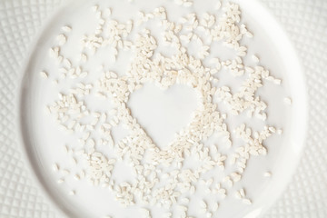 White short grain rice in a shape of heart spilled on a plate. Raw food ingredient background. Love for cooking concept