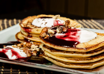 Homemade sweet pancakes with fruit jam, sour cream on a white plate. Breakfast with stack topped blueberry jam and walnuts.