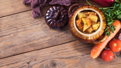 Vegetable and meat stew in crock with raw fresh vegetables. Top view. Copy space