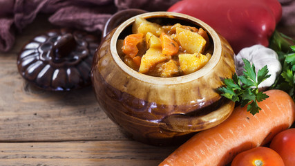 Vegetable Stew in Brown Pot with Raw Vegetables on Wooden background