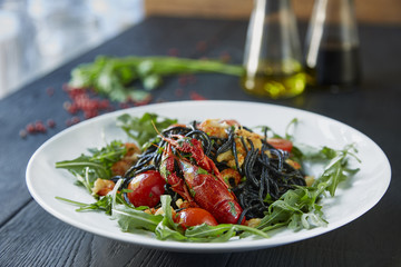 Black spaghetti with crayfish, fresh green arugula, cilantro, pepper and olive oil on a dark wooden table. 