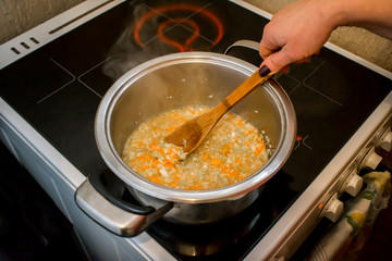 chopped soup ingredients: carrots, onions and celery cooking in a stainless steel pot