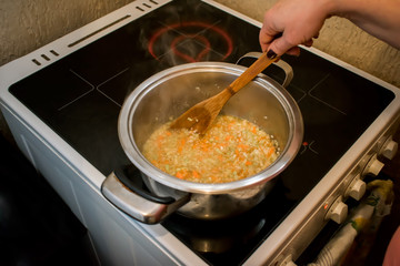chopped soup ingredients: carrots, onions and celery cooking in a stainless steel pot