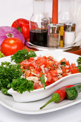 Salsa - a salad of fresh tomatoes and onions, seasoned with vegetable oil on a white salad bowl, decorated with parsley on a background of vegetables and cutlery