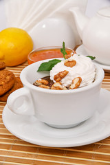 Hot chocolate with whipped cream and walnuts, decorated with mint leaves in a white cup on a decorative tablecloth