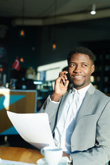 Confident banker with smartphone and paper calling in the morning