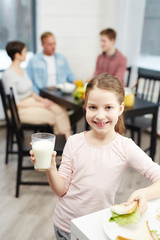 Healthy girl with glass of milk and sandwich looking at camera