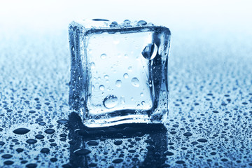 Transparent ice cube with reflection on blue glass with water drops