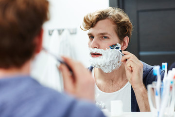 Attractive man shaving his beard in bathroom