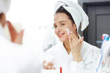 Young female applying cream on her face