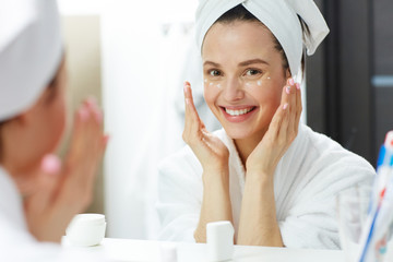 Happy woman with toothy smile pampering eye-cream