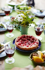 Strawberry cake surrounded by glasses of red wine and flowers