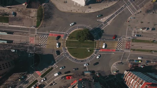 Top view, aerial of urban roundabout way busy with traffic, tram road, bicycle lane and various restricted marks on it.