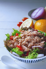 tuna fish salad with lettuce, onion, lemon and tomatoes on white wooden table in background.