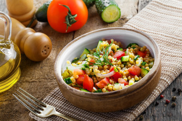 Healthy salad for breakfast made of couscous, tomatoes, cucumber and onion on a table. Traditional Israeli Ptitim meal. Moroccan cuisine food.
