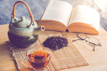 A cup of tea with tea pot and dride tea leaf  with reading book on table