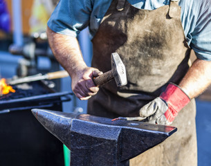 Blacksmith hammering iron rod on anvil in background fire