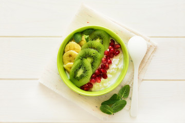 Healthy breakfast: fresh cottage cheese with kiwi, banana, garnet seeds and honey decorated mint leaves on white wooden table. Selective focus